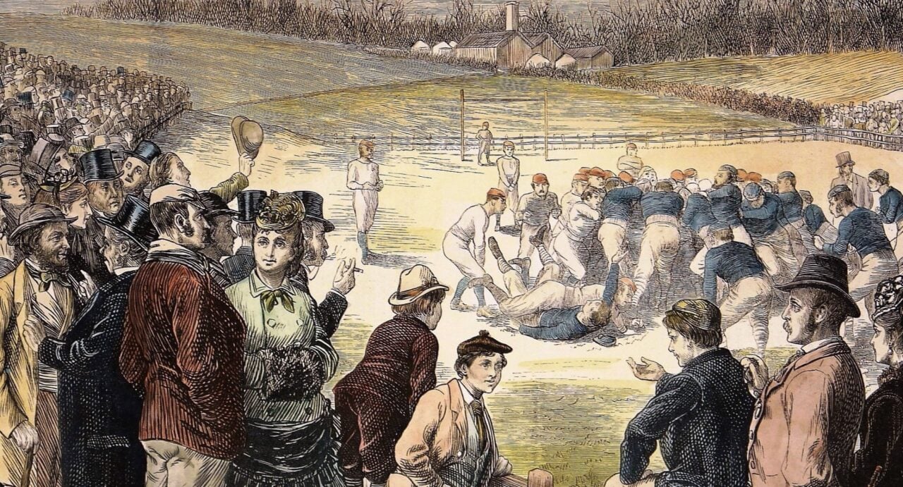 A view of the action from the first rugby international, Scotland v England, played at Raeburn Place in Edinburgh in 1871. The players are in a scrum in the middle, the crowd watches from behind fences