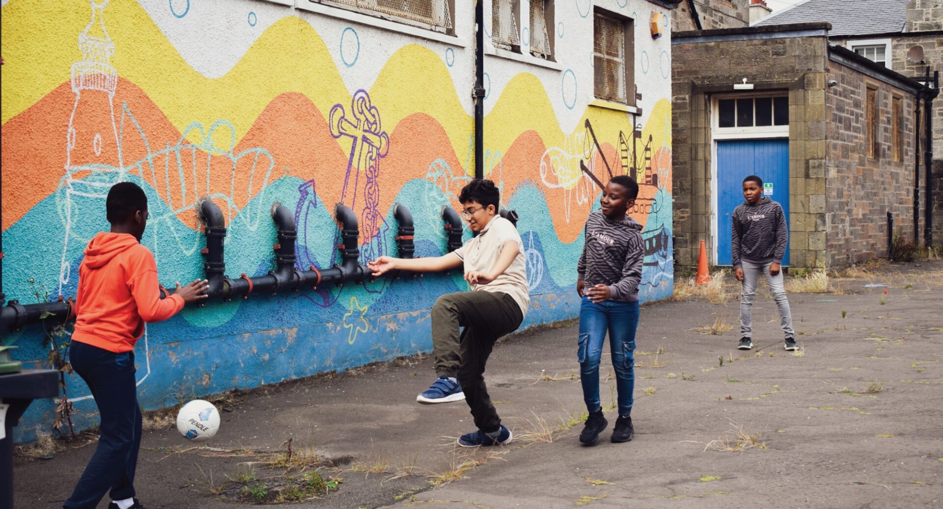 Children playing football in the playground, with a brightly coloured abstract nautical mural in the background