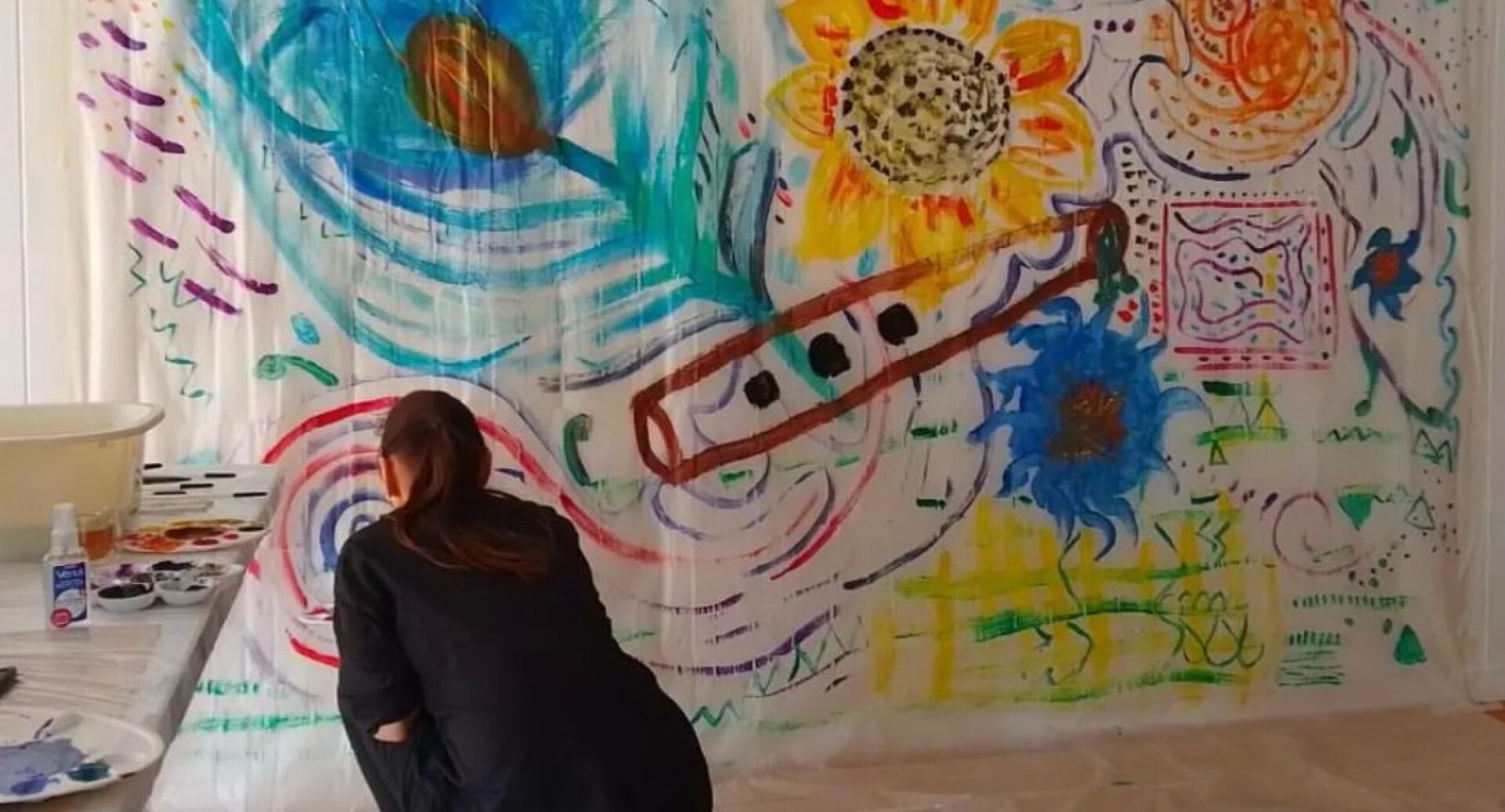 A woman kneeling in front of a sheet on which flowers and various symbols have been painted