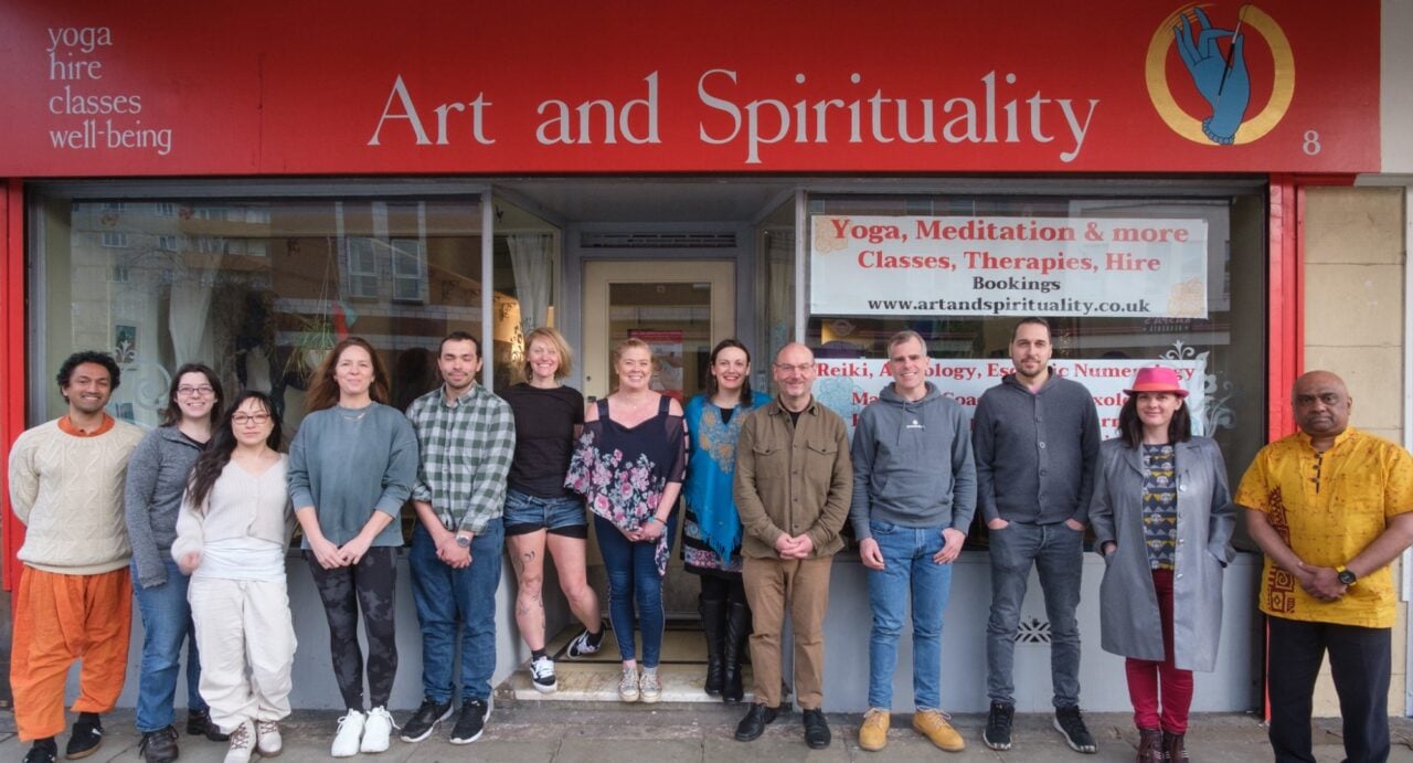 The thirteen Art and Spirituality facilitators standing on the pavement outside their building