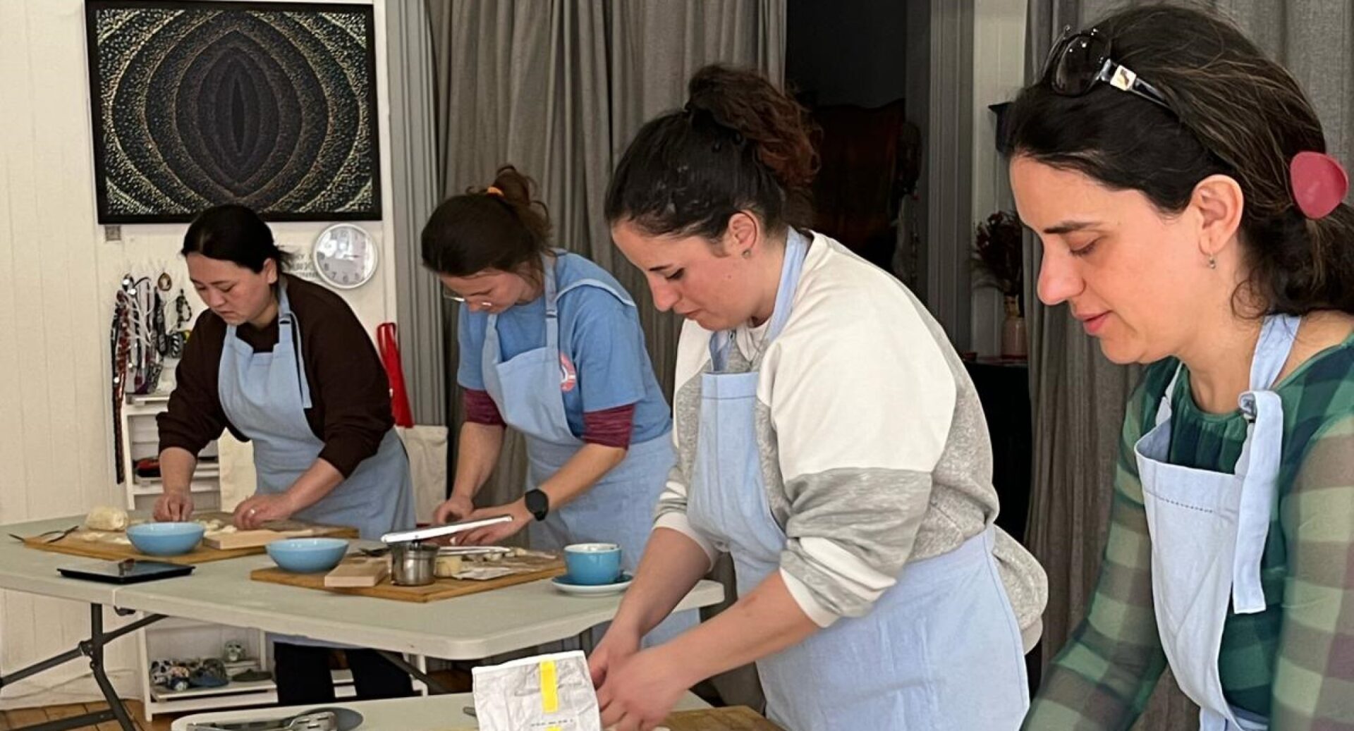 Four women wearing aprons preparing food in a cooking class