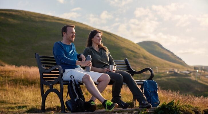 Couple enjoying a coffee sitting on a bench with Pentland Hills in background