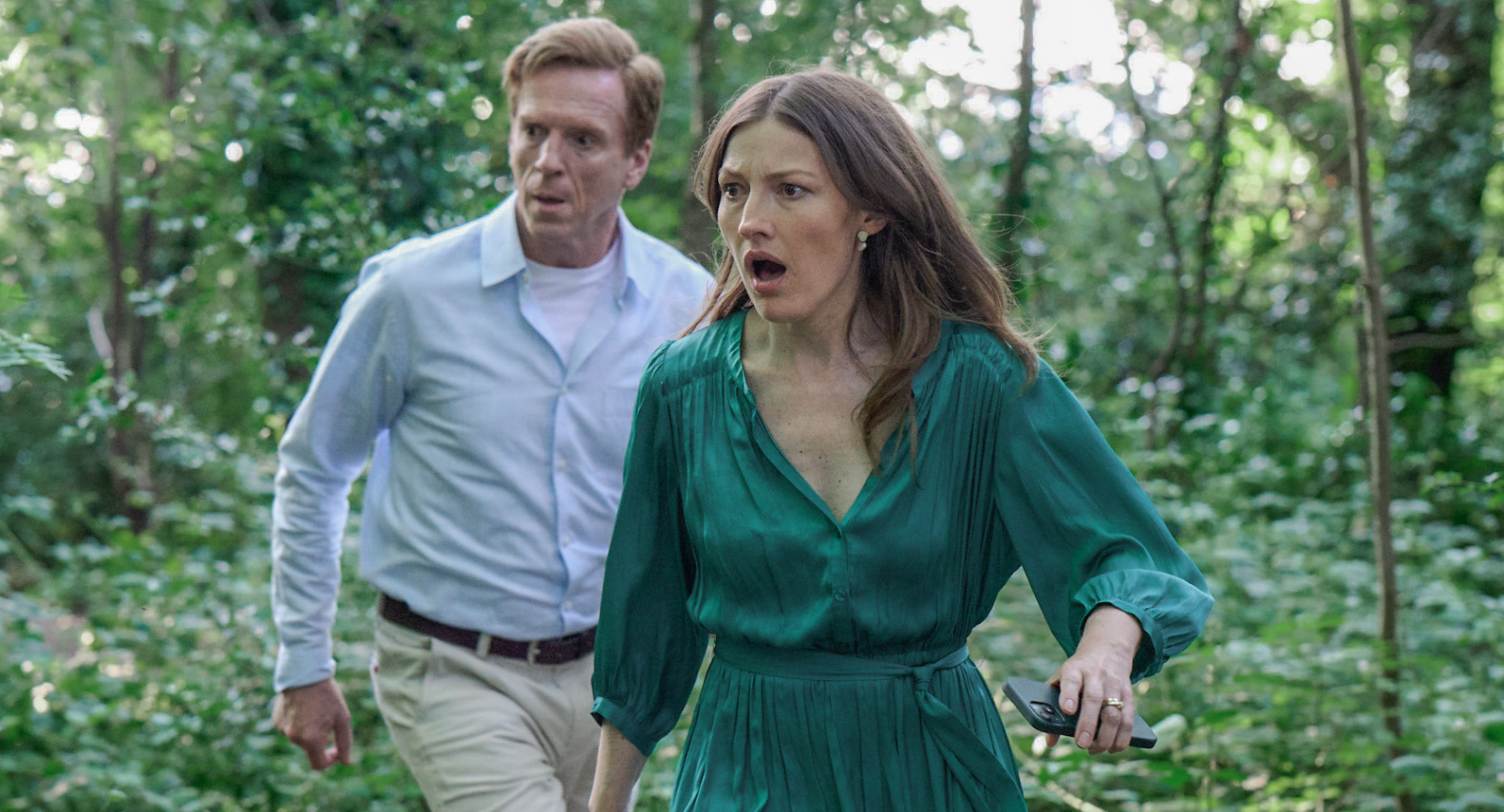 Damian Lewis and Kelly Macdonald exploring wooded area.