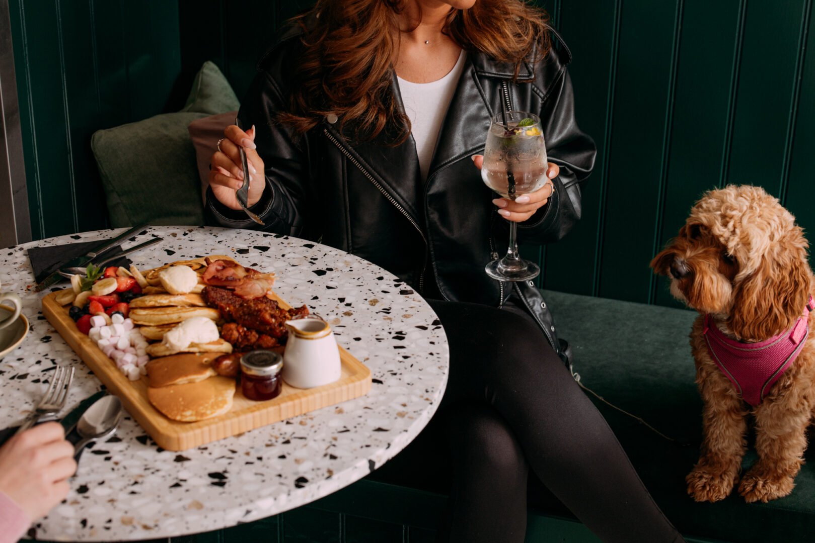 Lady with a sharing platter of pancakes and sweet treats with a dog sitting looking on