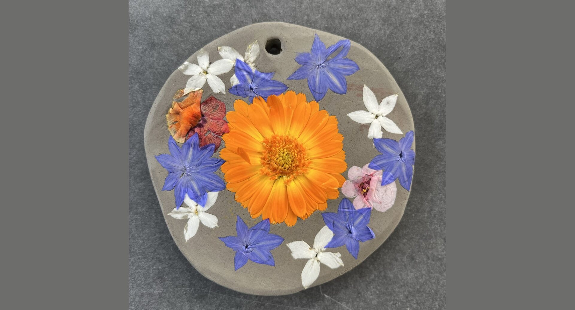 A circular ceramic disc with pressed orange, blue and white flowers on the surface