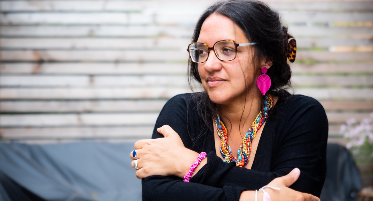 Hannah Lavery, wearing glasses, a multicoloured necklace, a pink bracelet, pink leaf earring and silver rings, gazes off camera