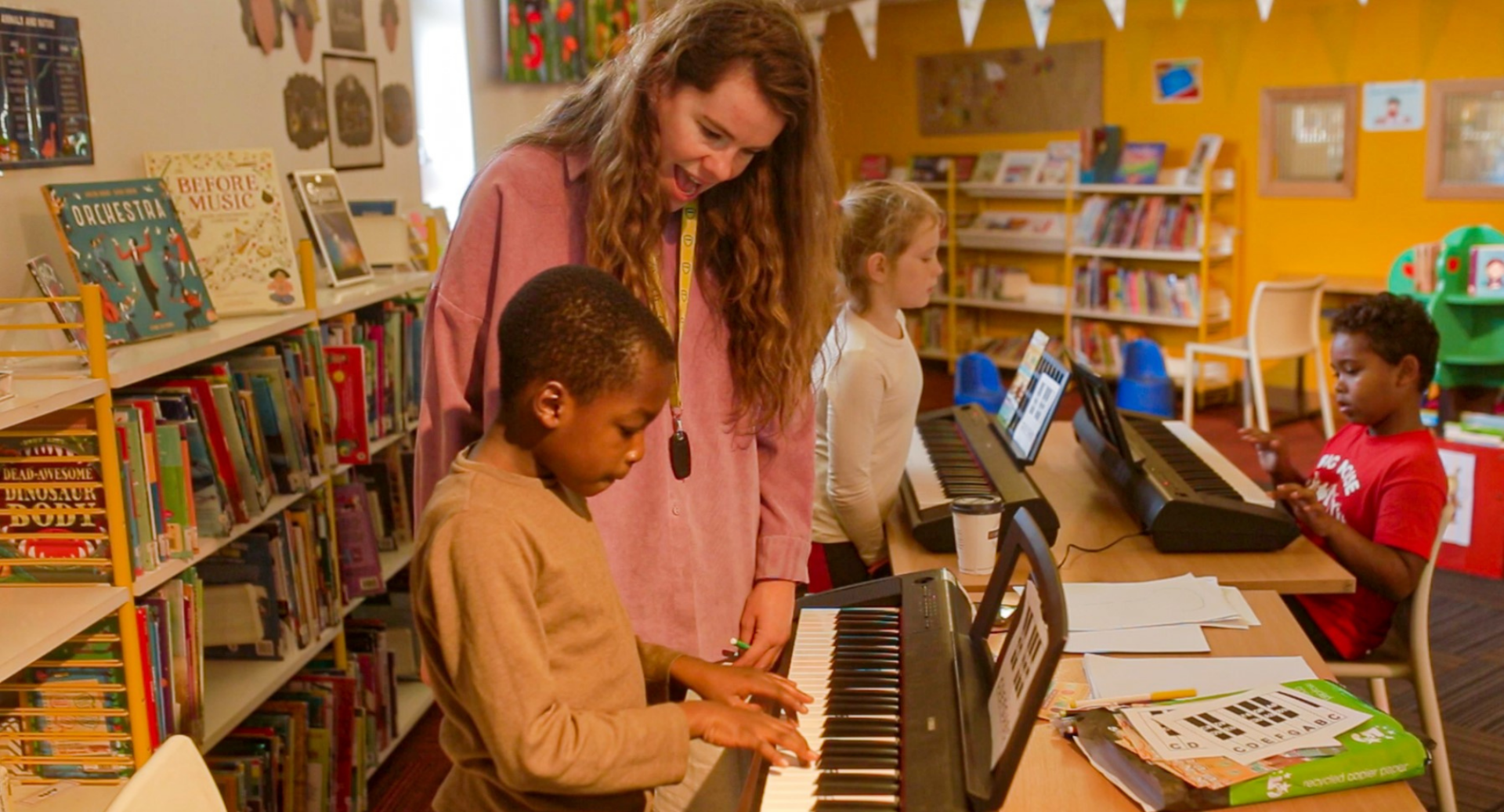 Children playing on piano keyboards in a room lined with books