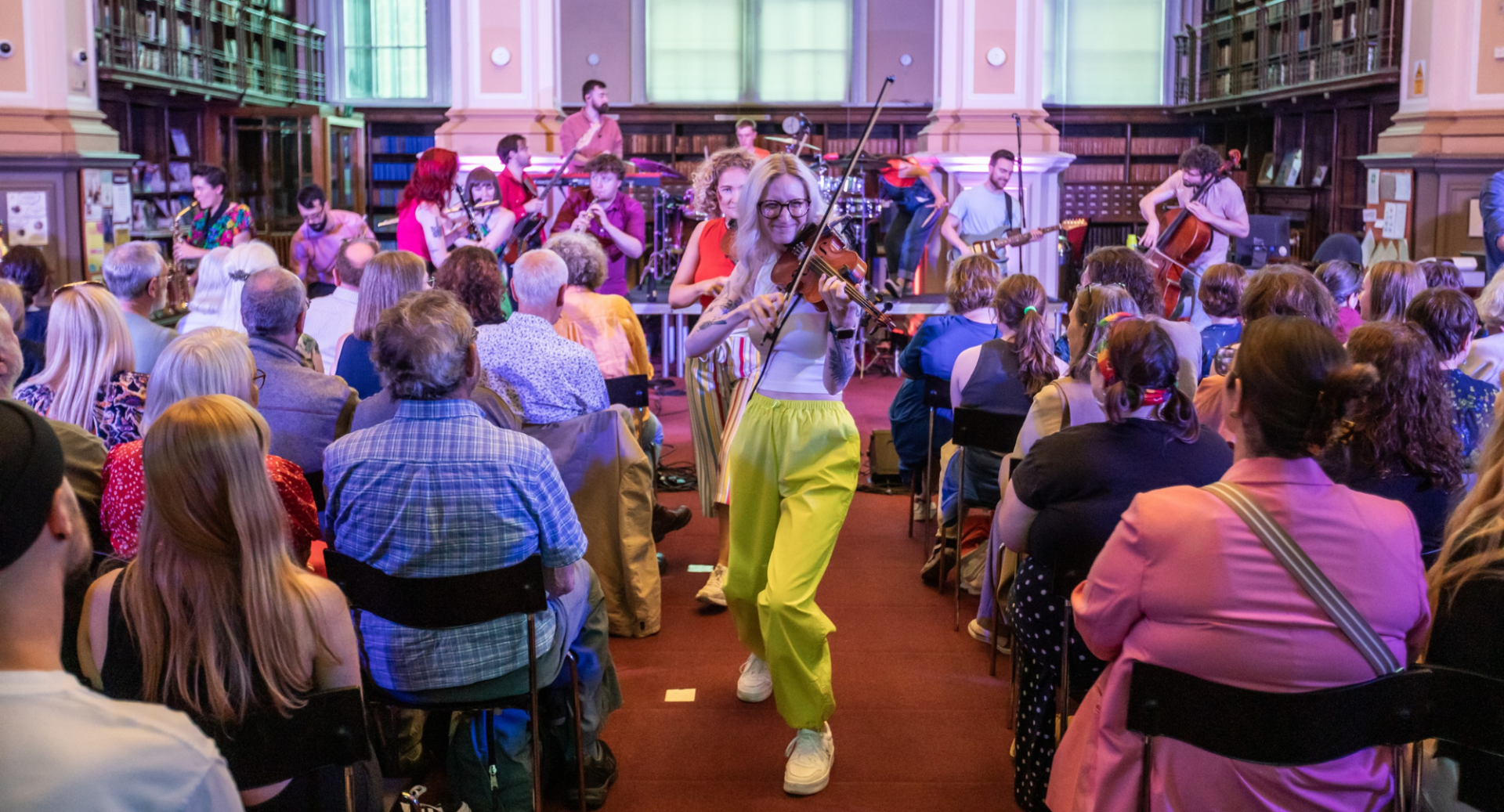 A crowd watch the Tinderbox Orchestra, as the musicians begin to file up the middle aisle playing their instruments