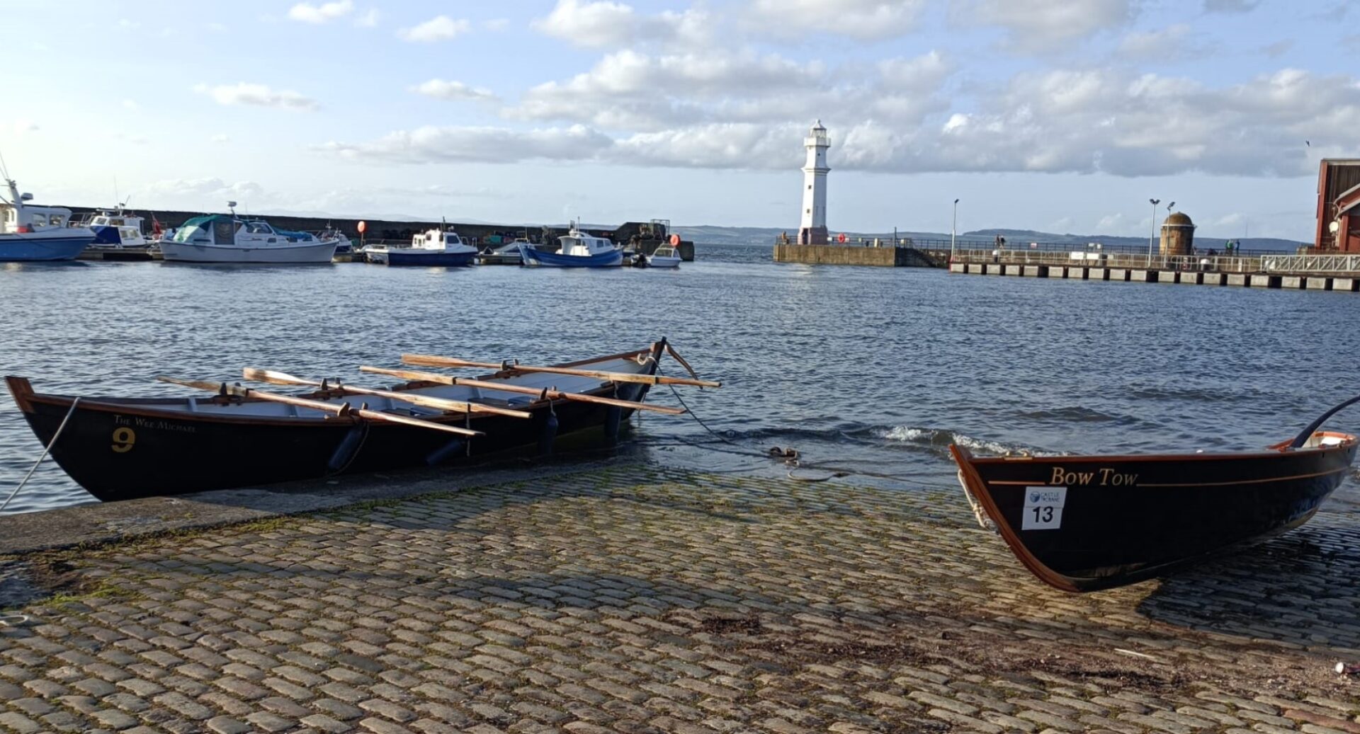 Newhaven Harbour with two skiffs lying on shore and the lighthouse and other boats in the background