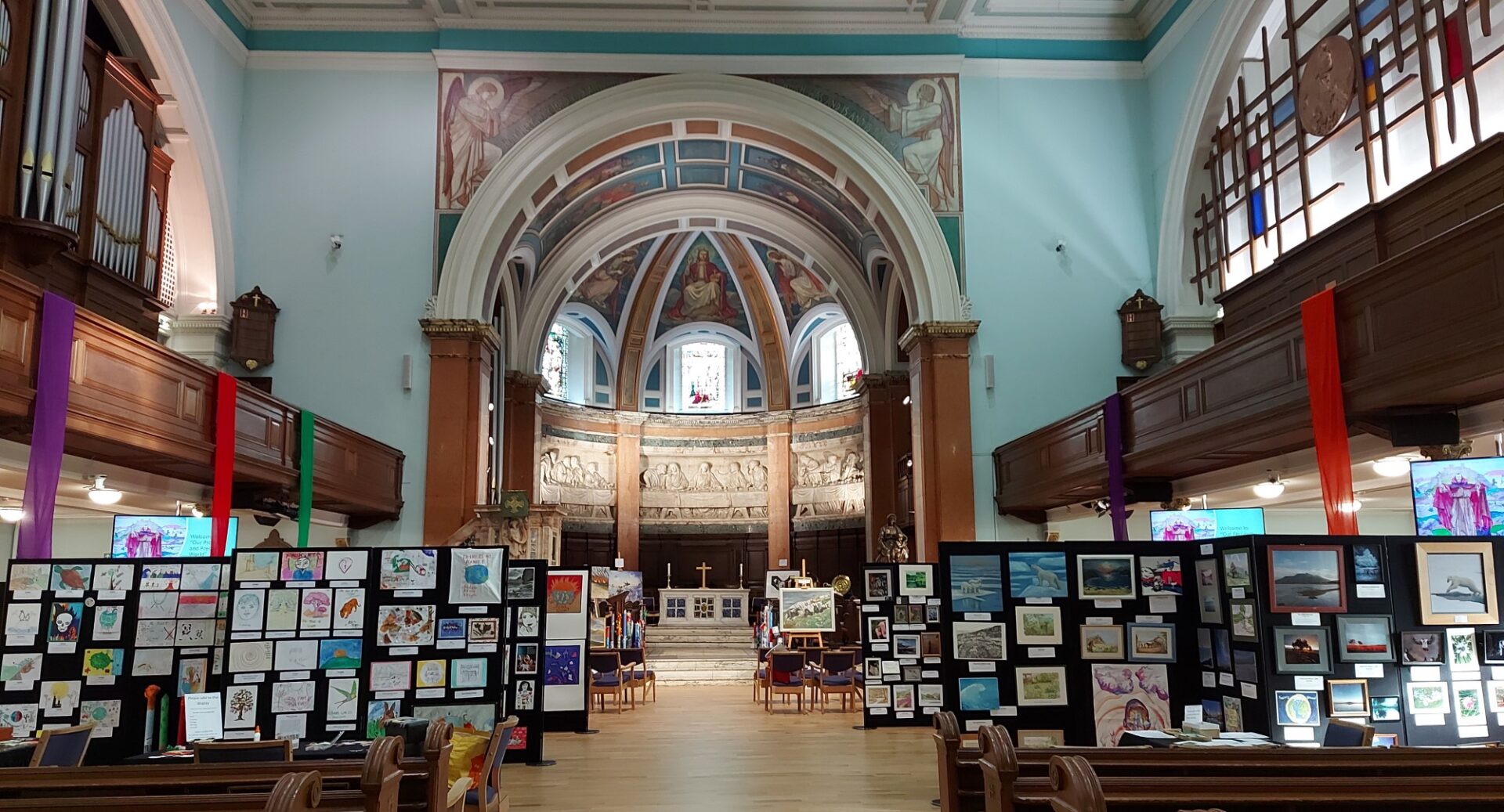 The interior of St Cuthbert's Church from the aisle, with pews on either side and artworks displayed on boards at the front