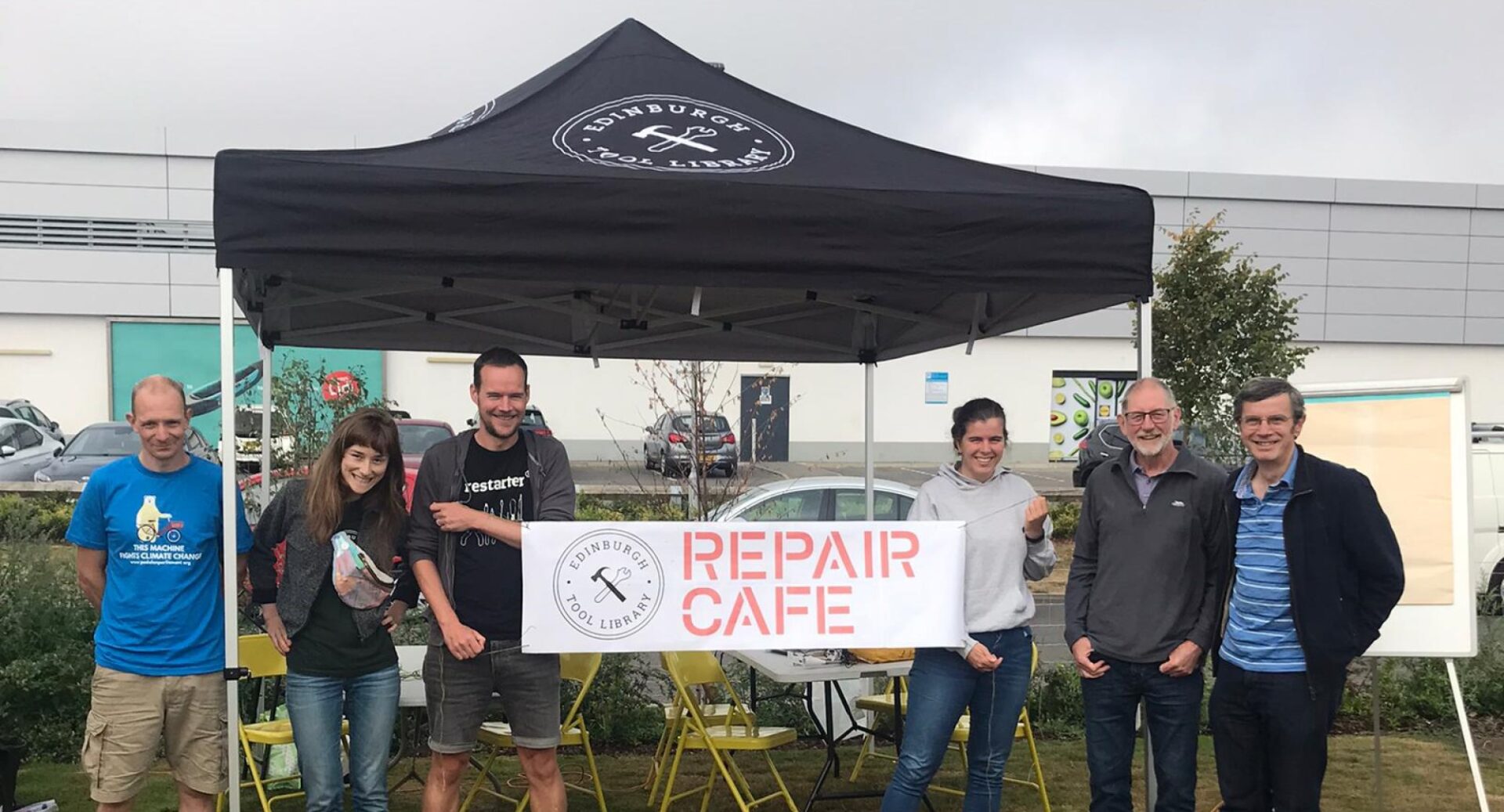 A group of people standing underneath the black Repair Cafe gazebo