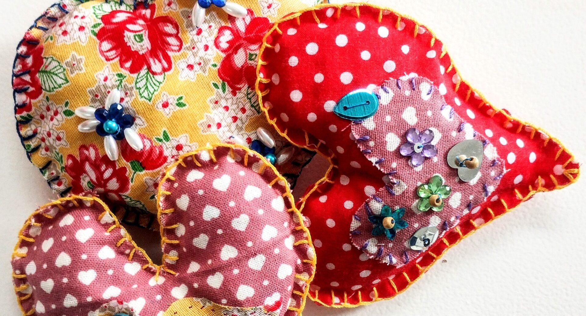 Three fabric hearts, in yellow floral, red and white spotted, and pink and white hearts materials