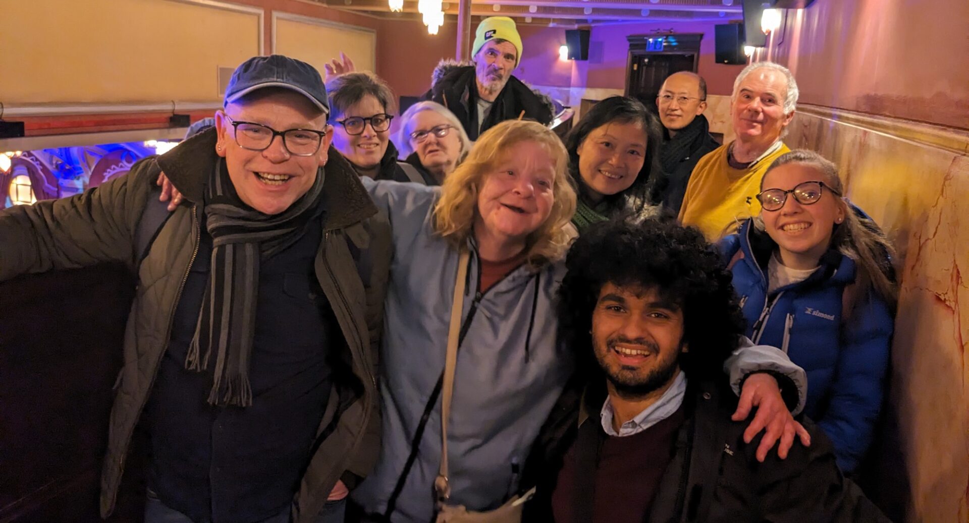 A group of Whale Arts members huddled together in a narrow corridor and smiling at the camera