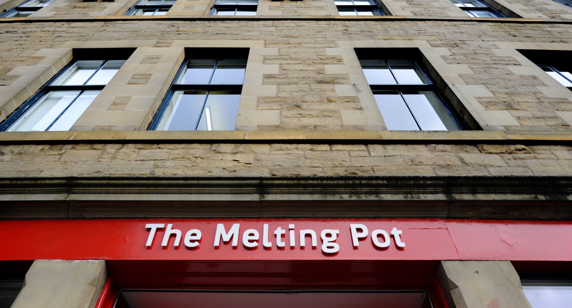 An exterior shot of part of the Melting Pot building showing the red sign and windows above