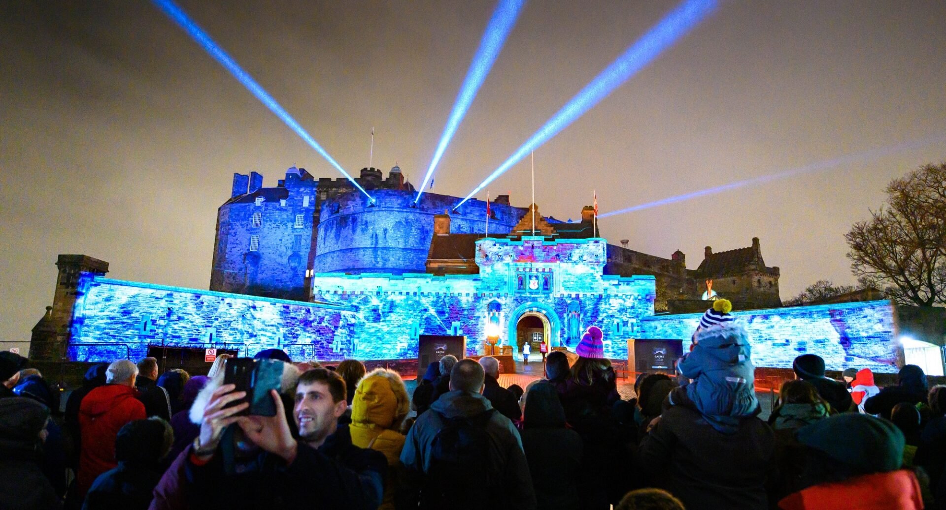 Edinburgh Castle lit up blue, with crowds in the foreground