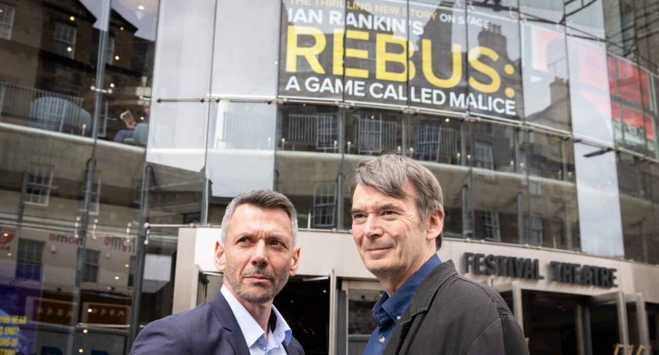 Gray O'Brien and Ian Rankin wearing jackets and open necked shirts, and standing outside the Festival Theatre, which displays a poster for the show above the entrance