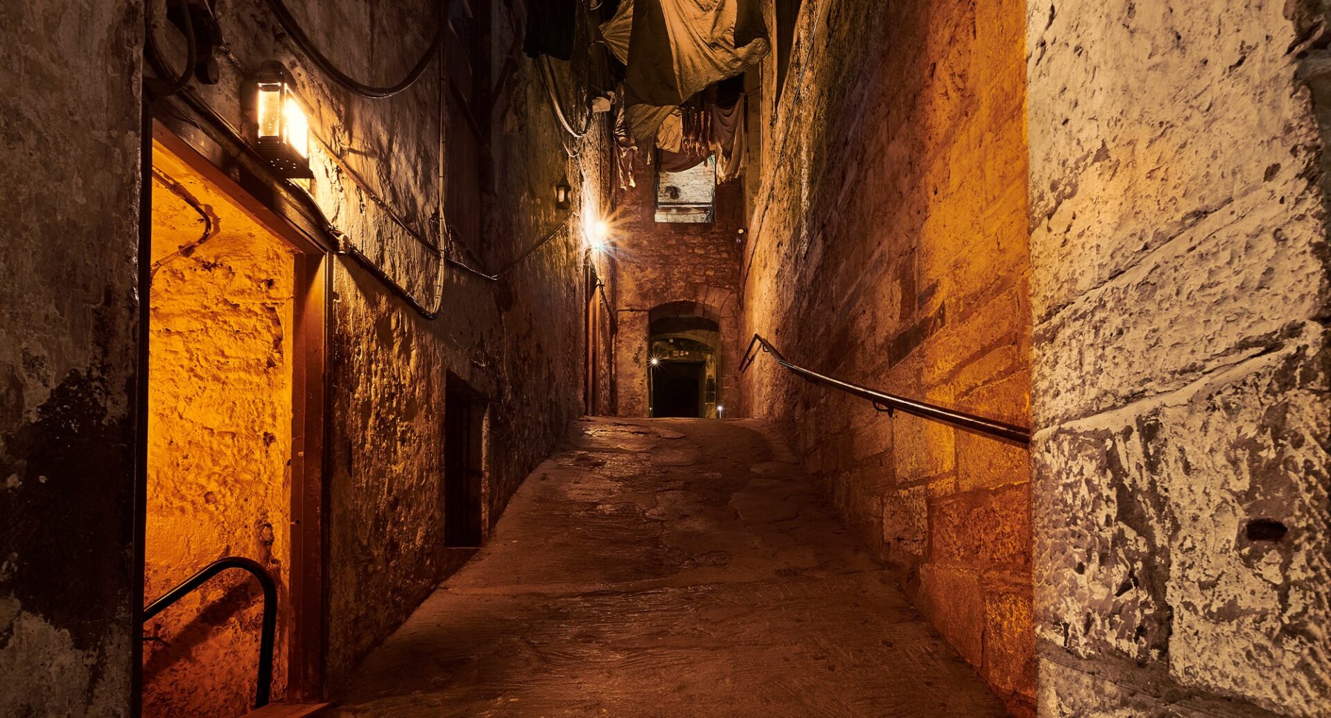 An eerie close lit by lanterns on one wall