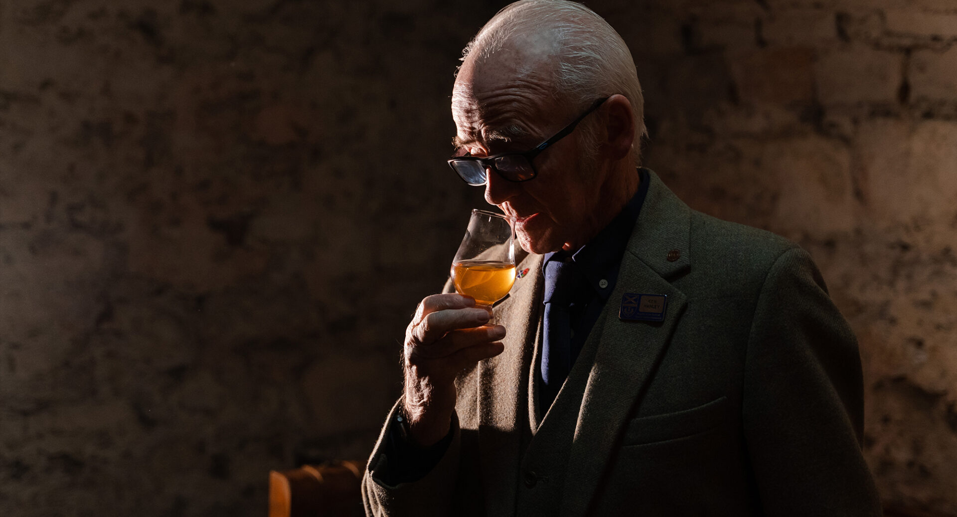 An elderly man in a suit sniffing a glass of whisky