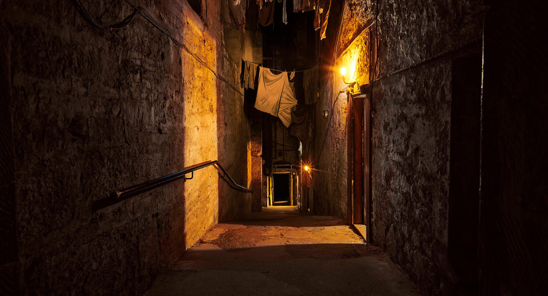 Washing hangs across a darkened close lit by a lantern on one wall