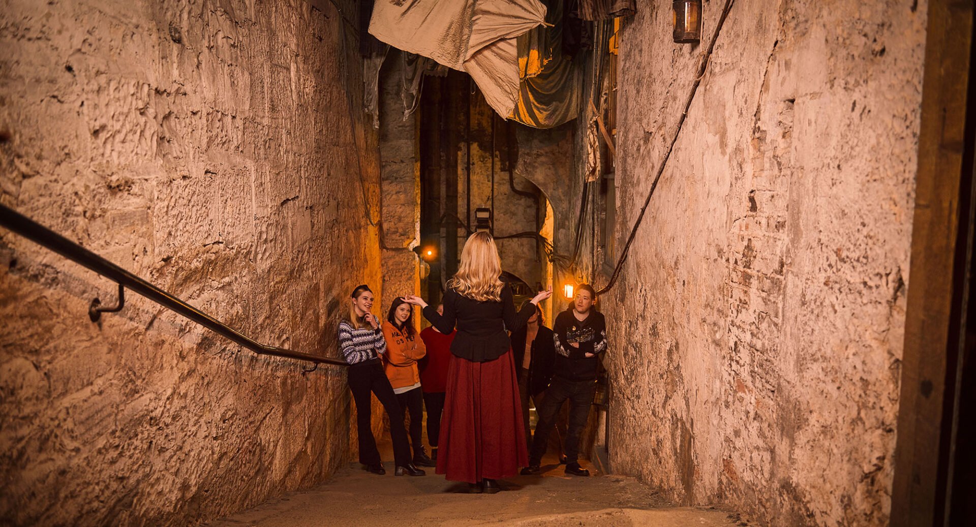 A tour guide with her back to the camera speaks to an audience while standing in a steep close