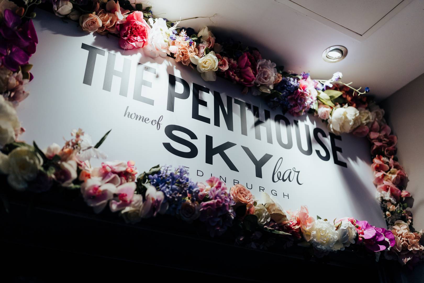 Sign for Penthouse home of the SKYbar with flowers around it