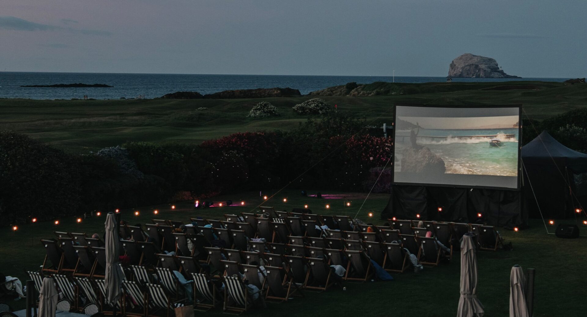 Deckchairs set up on lawn in front of large screen.