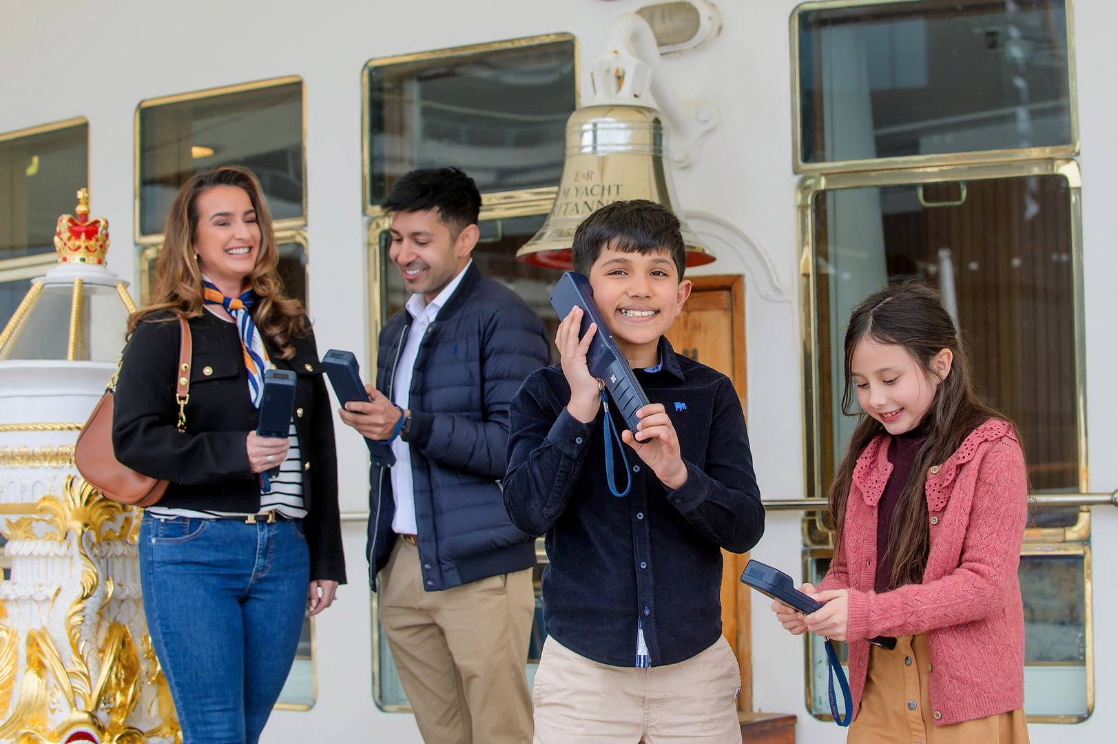 A family including a man, woman, little boy and girl are listening to an audio tour handset by Britannia's Bell. ,© Helen Pugh