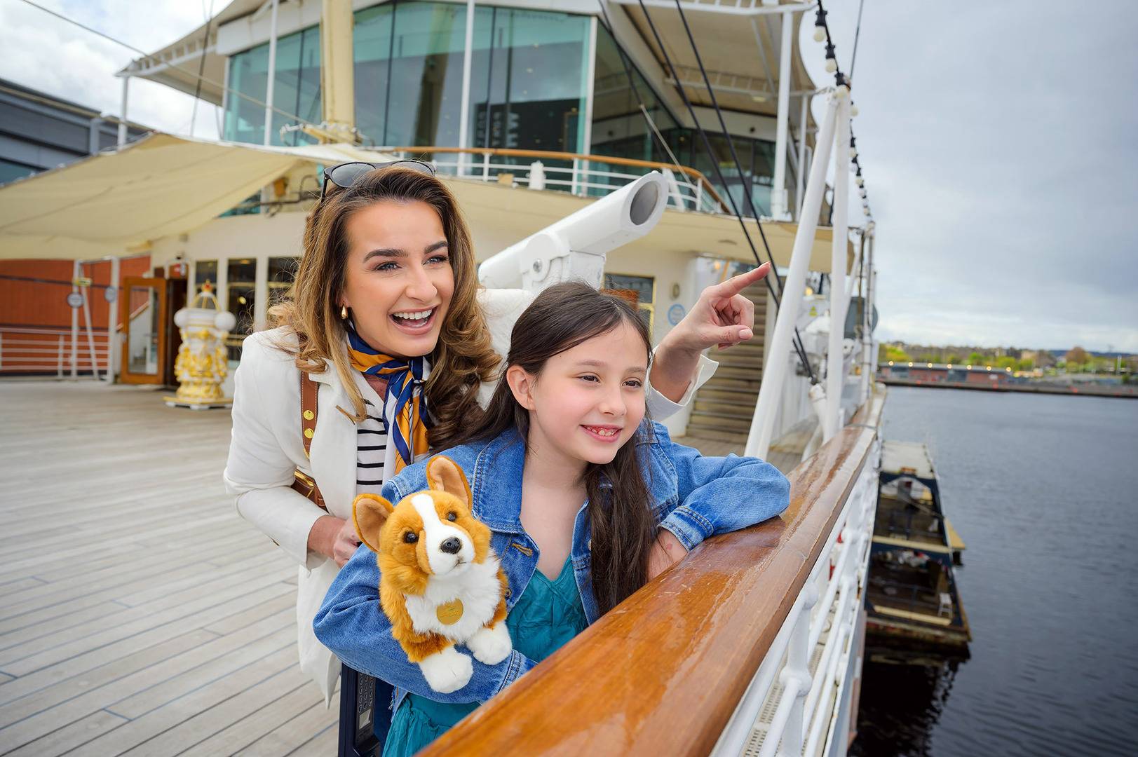 A woman and little girl are on the Verandah Deck at Britannia admiring the view. The girl is holding a cuddly Corgi dog toy.,© Helen Pugh