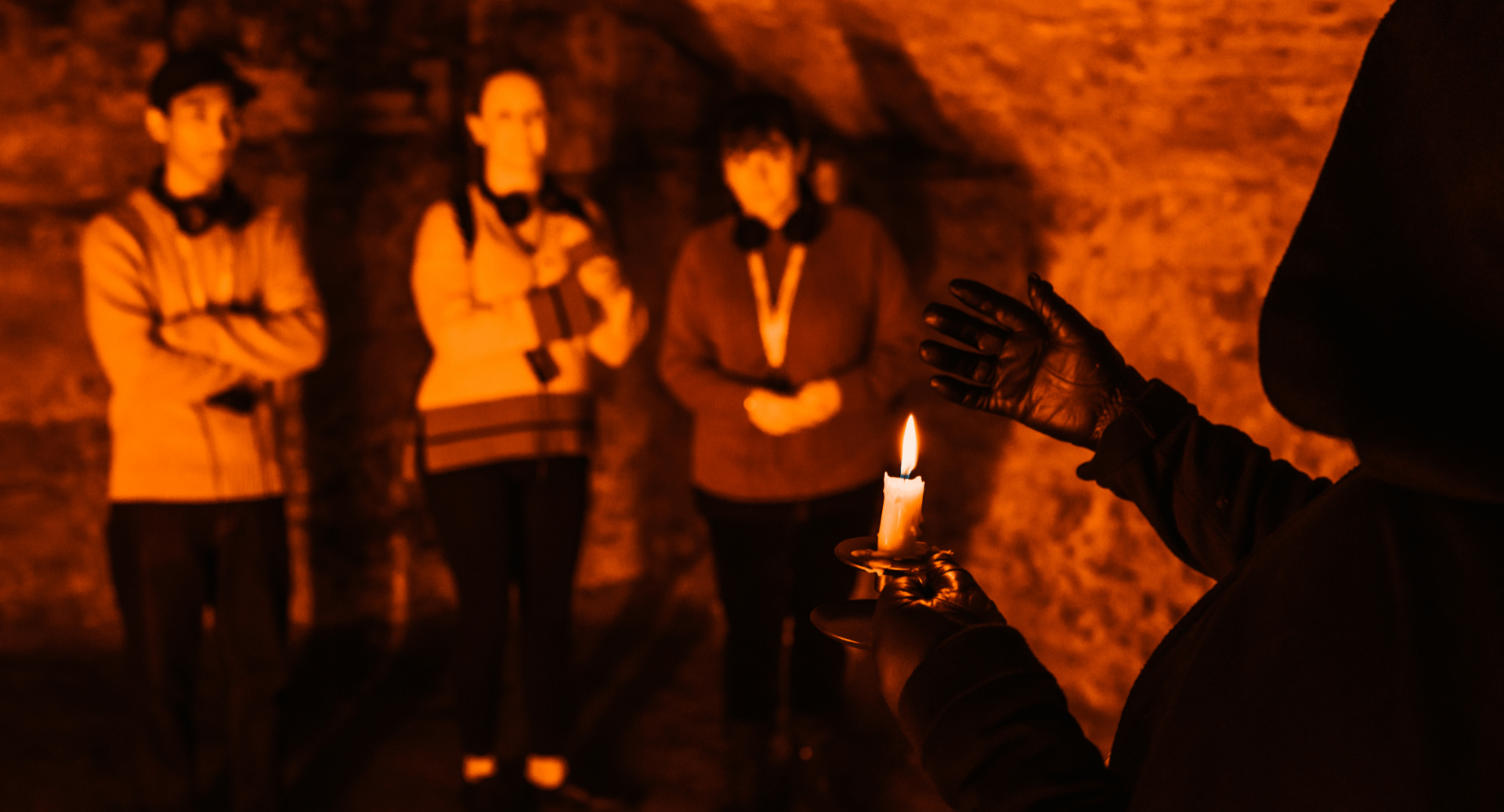 Hooded figure holding a torch in the Blair Street Vault with 3 people on the tour