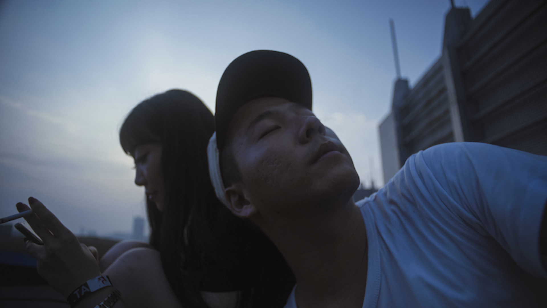 Man and women sitting down against blue sky.