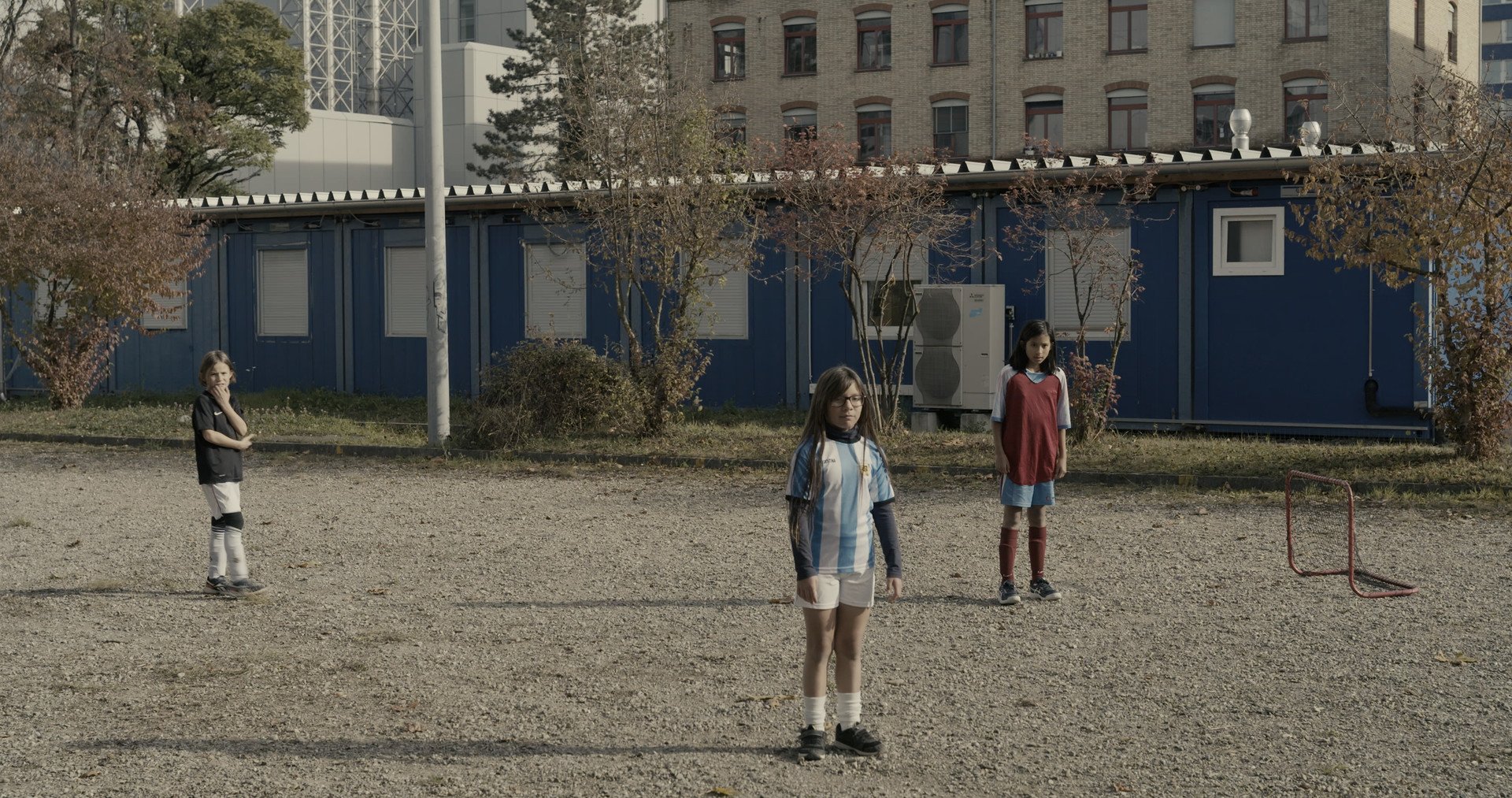 3 young girls in football strips standing beside small goalposts.