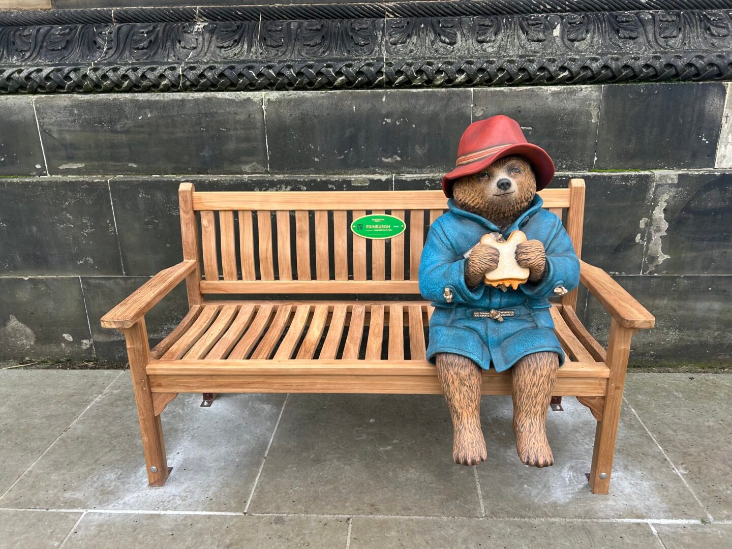 A statue of Paddington Pear with marmalade sandwich sitting on bench