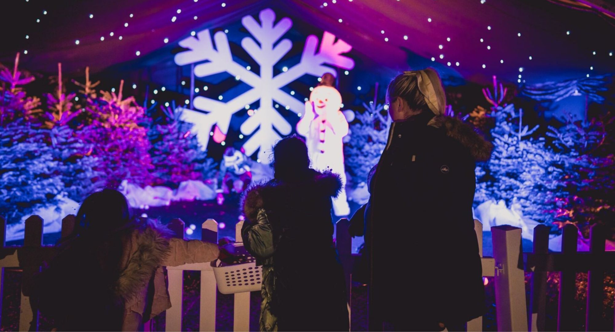 Adult and child looking at illuminated snowman standing in wintry forest.