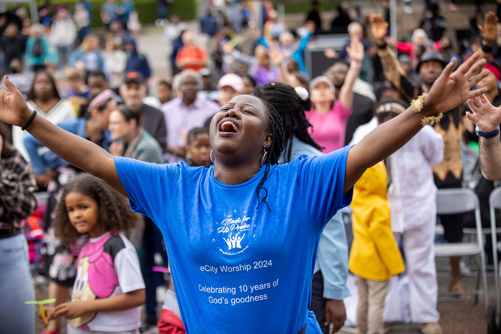 A performer in a blue tshirt with arms aloft. The crowd is in the background