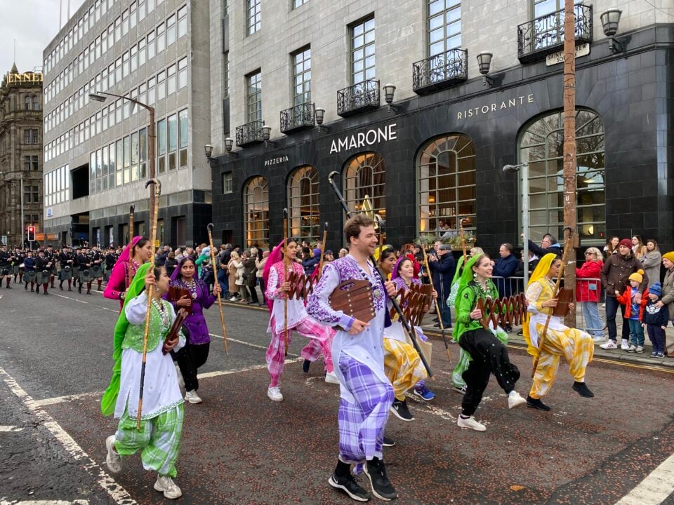 Crowd of musicians wearing colourful traditional Indian clothing walking through busy street