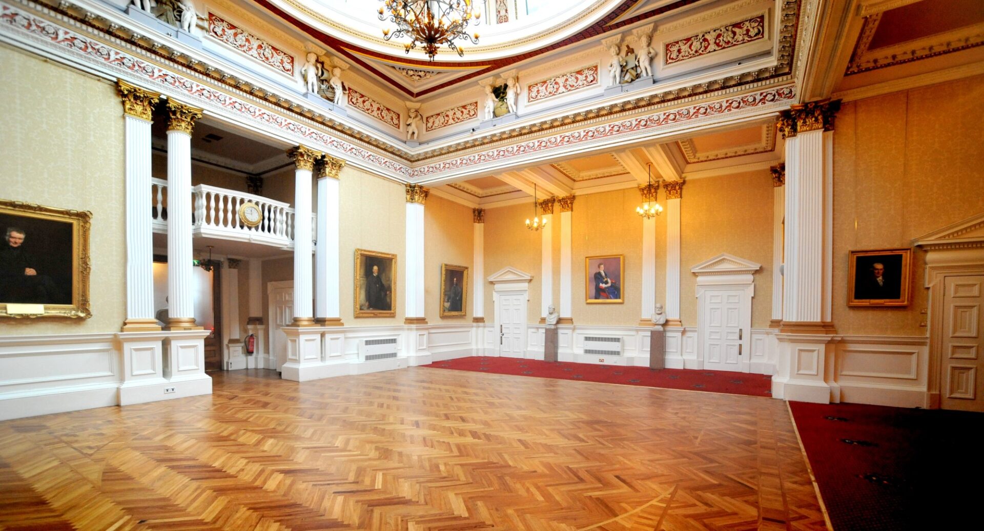 An interior shot of Merchants Hall showing a parquet floor, white and gilt porticos and cornices, a chandelier and a glimpse of a cupola