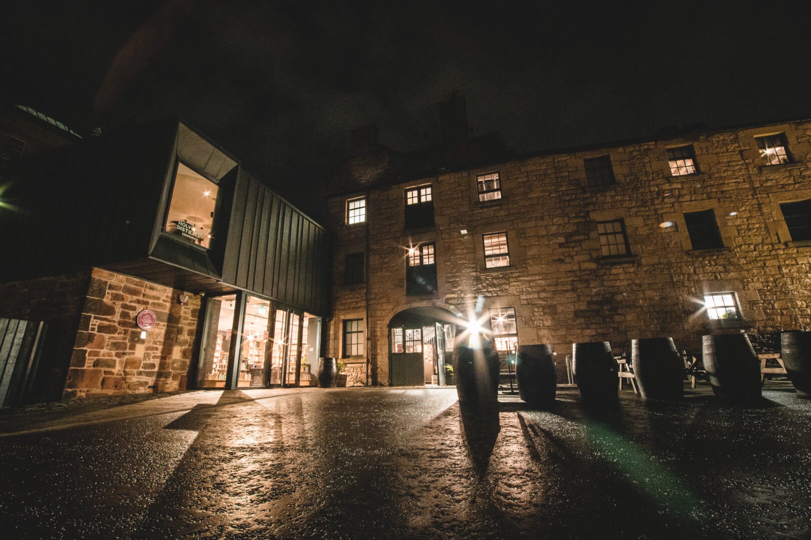 Exterior of Holyrood Distillery at night, with lights illuminating the building.