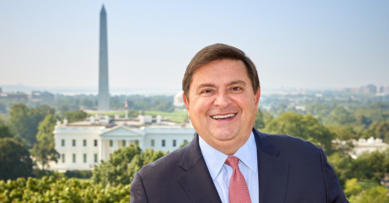 Headshot of Stewart McLaurin, wearing a suit and tie, with the Washington Memorial and White House in the distance