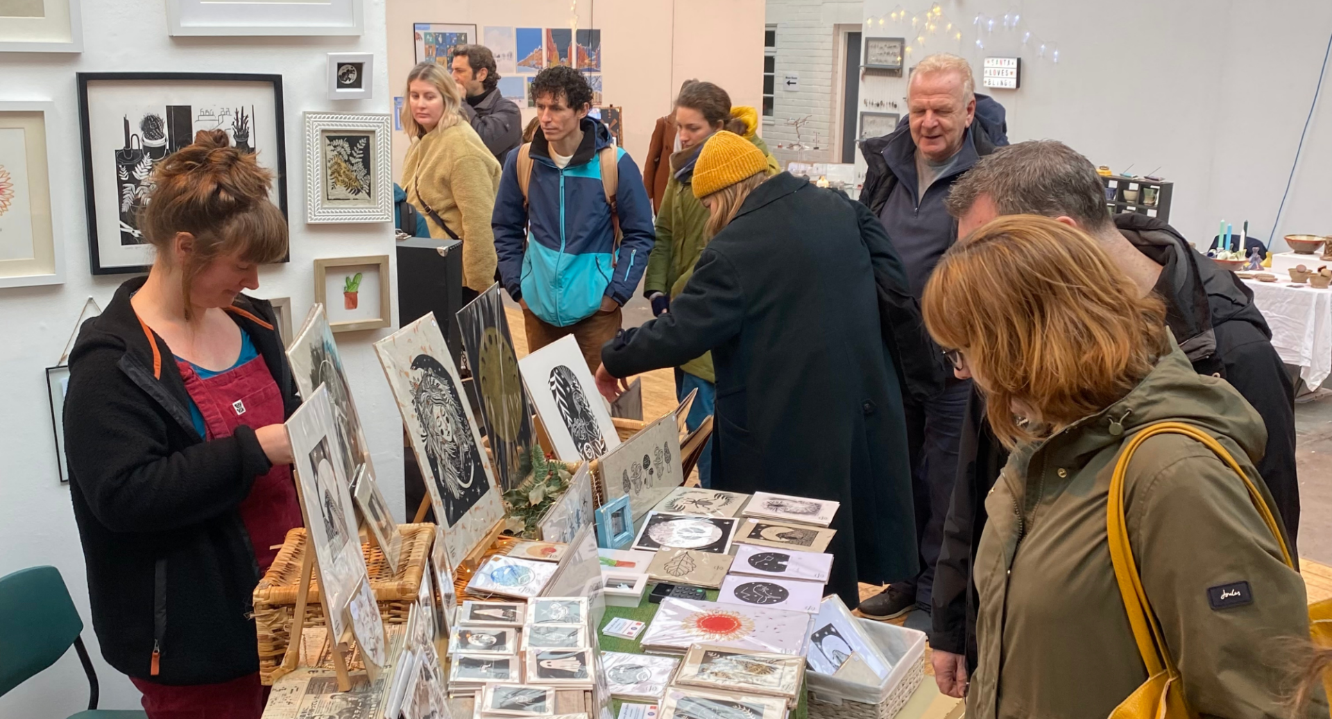 Room of people browsing a craft stall, displaying a range of posters and cards.