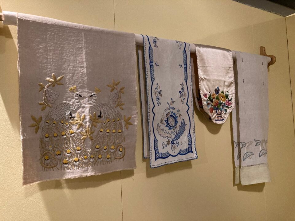 4 embroidered garments displayed on wooden pole, hanging on wall.