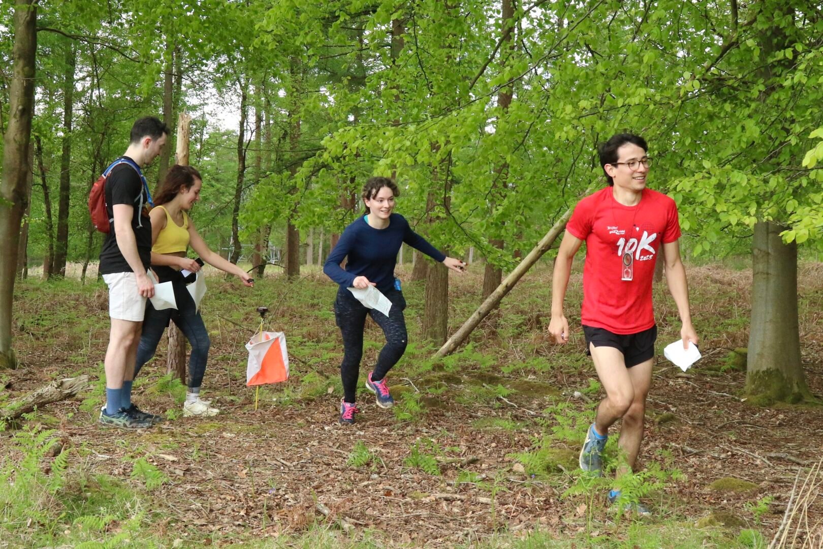 4 people running through a wooded area, navigating an orienteering course together.