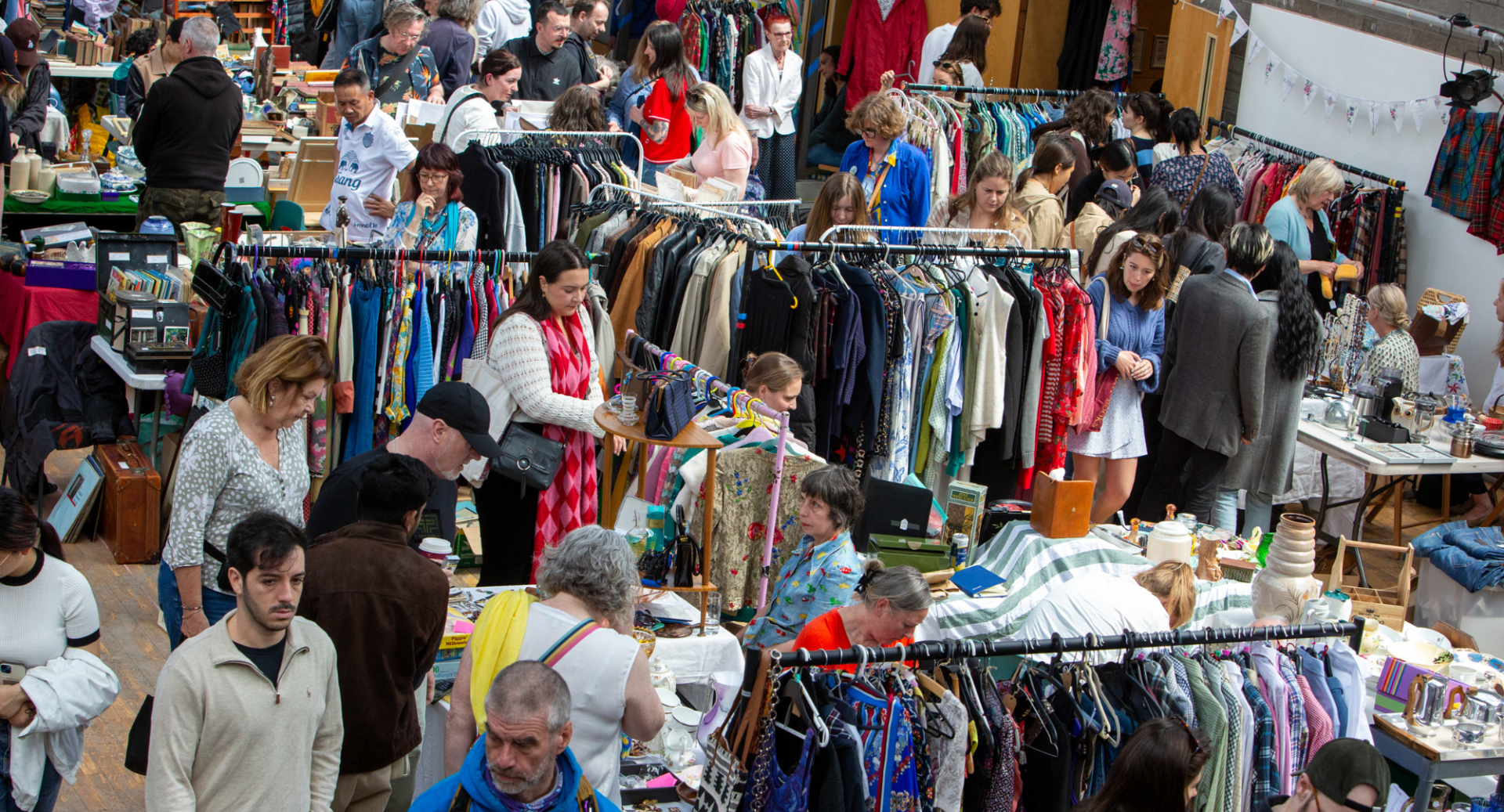 Room full of people browsing stalls and racks of clothing.