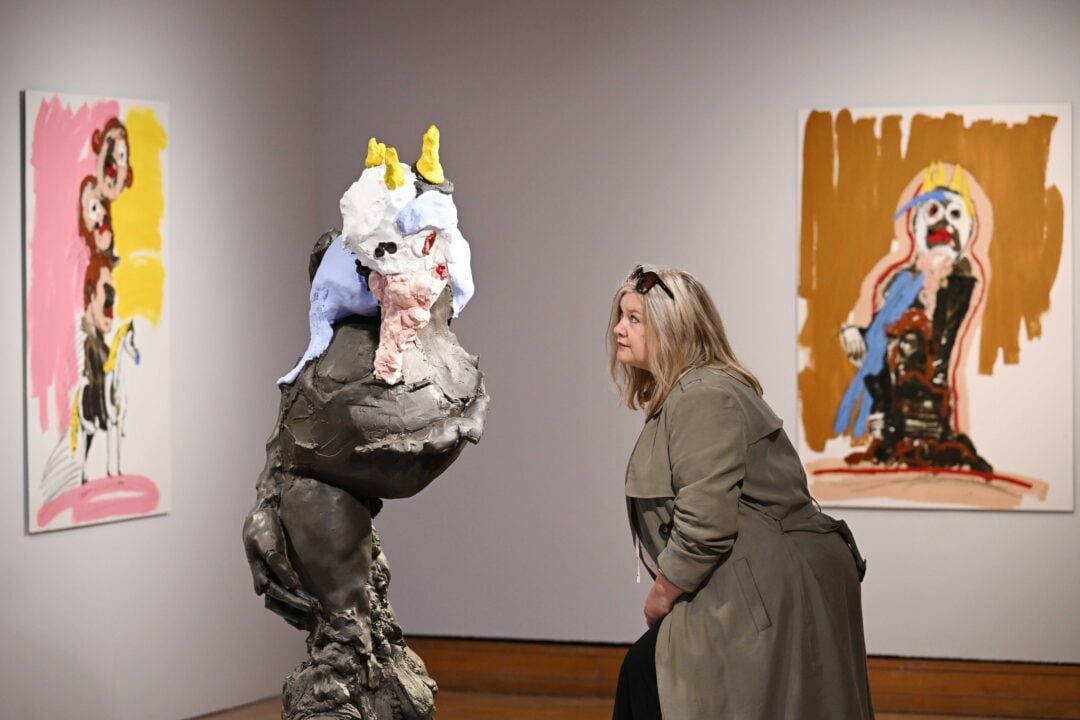 Women looking closely at sculpture. Walls in background have one painting on each.