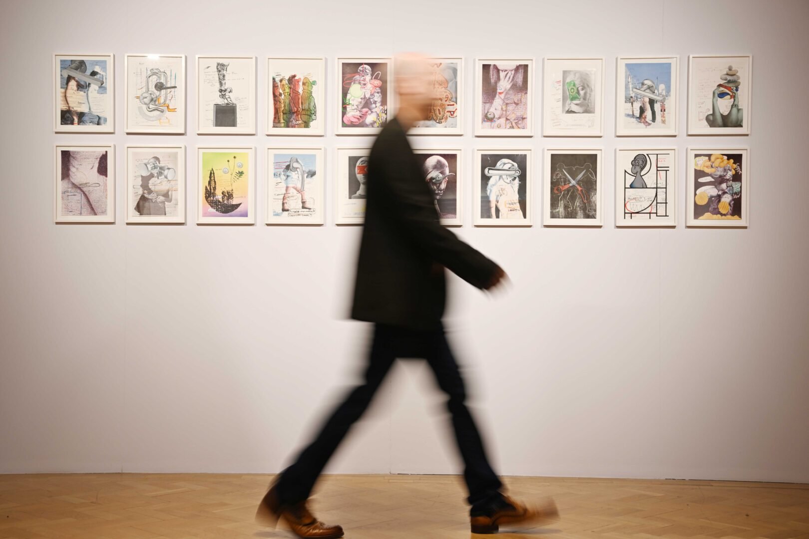 Blurred image of man walking past a wall decorated with a series of paintings.