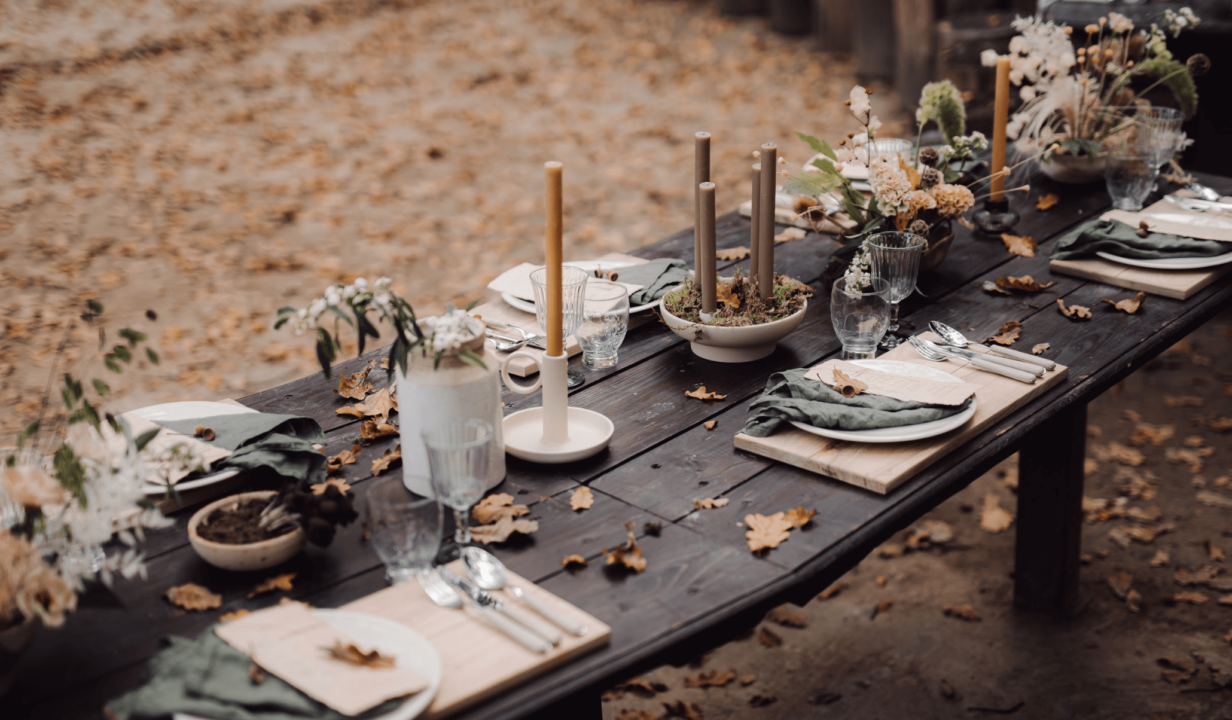 Long wooden table decorated with dinner settings, candles and foliage.