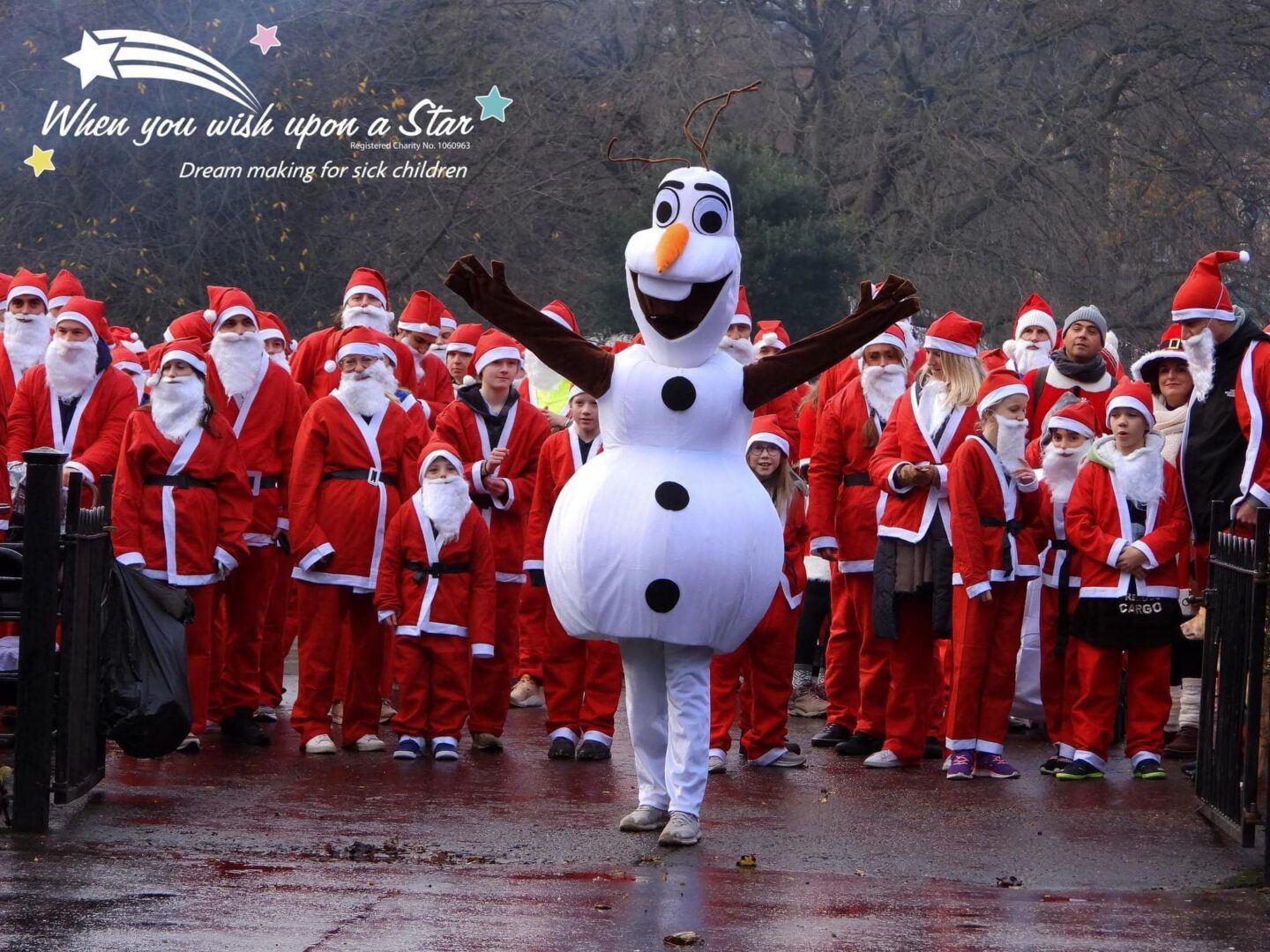 Person in a snowman costume standing in front of a crowd of people, all dressed in Santa costumes.