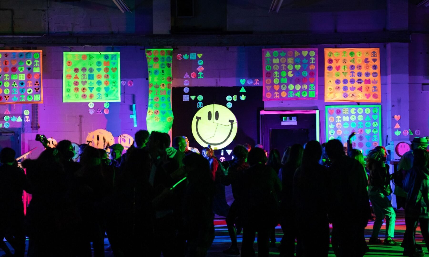 Group of people looking at glow in the dark smiley face and various painted images on wall.