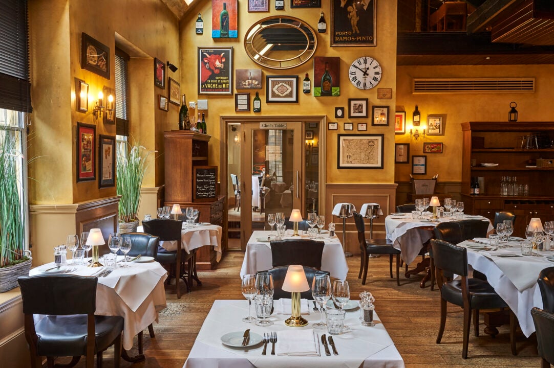 Interior of restaurant, with tables set with plates, cutlery and table lamps.