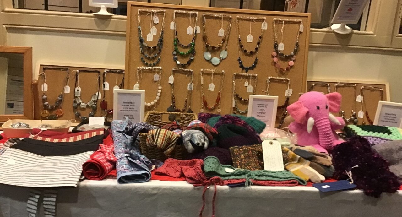 Table with displays of handmade gifts, including soft toys, necklaces and scarfs.