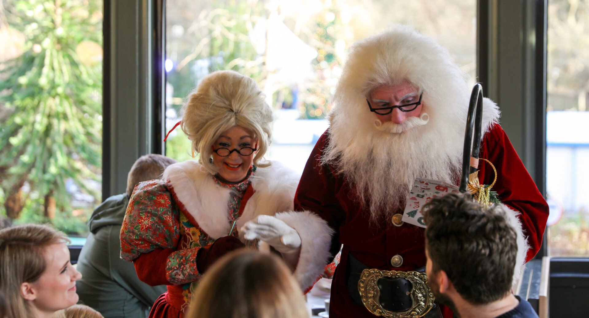 Couple dressed in red and white costumes talking to a group of people seated at a table.